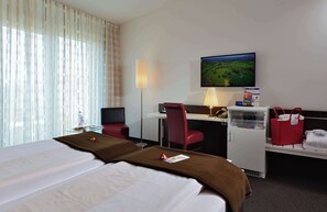 Una habitación de hotel con cama, escritorio, silla, televisor y un refrigerador pequeño.