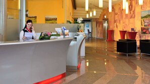 Zona de recepción de un hotel con diseño moderno, que incluye un mostrador de recepción, un área de descanso y un pasillo que conduce a otras habitaciones.