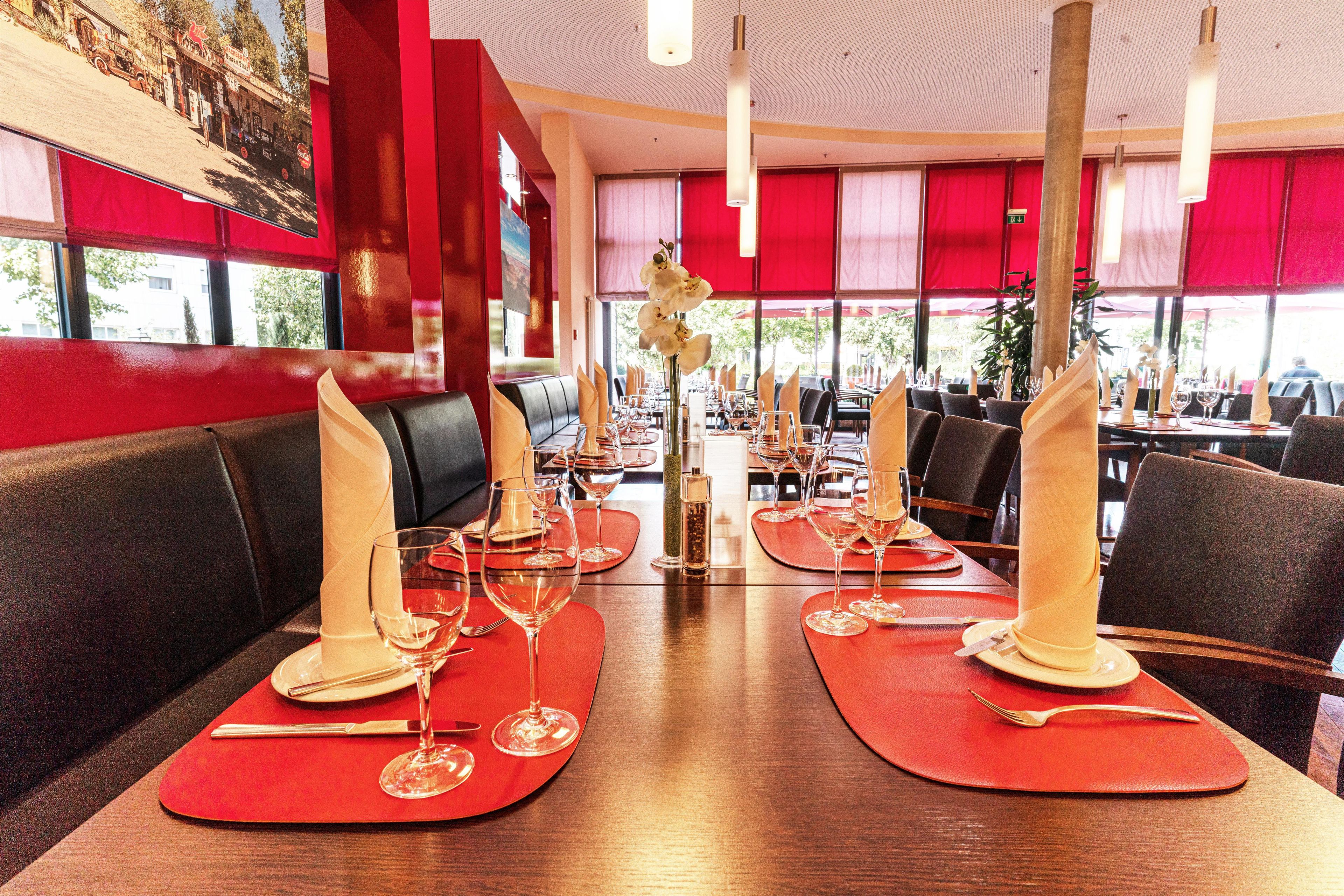 A restaurant interior with booths, red table settings, and a view of the street outside.