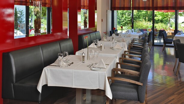 Un restaurante con mesas largas, manteles blancos y asientos de cuero negro.