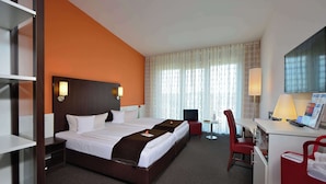 Habitación de hotel con una cama grande, un escritorio con silla, televisor y ventana con cortinas.
