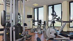 Un gimnasio con máquinas de cardio, máquinas de pesas y una televisión en la pared.