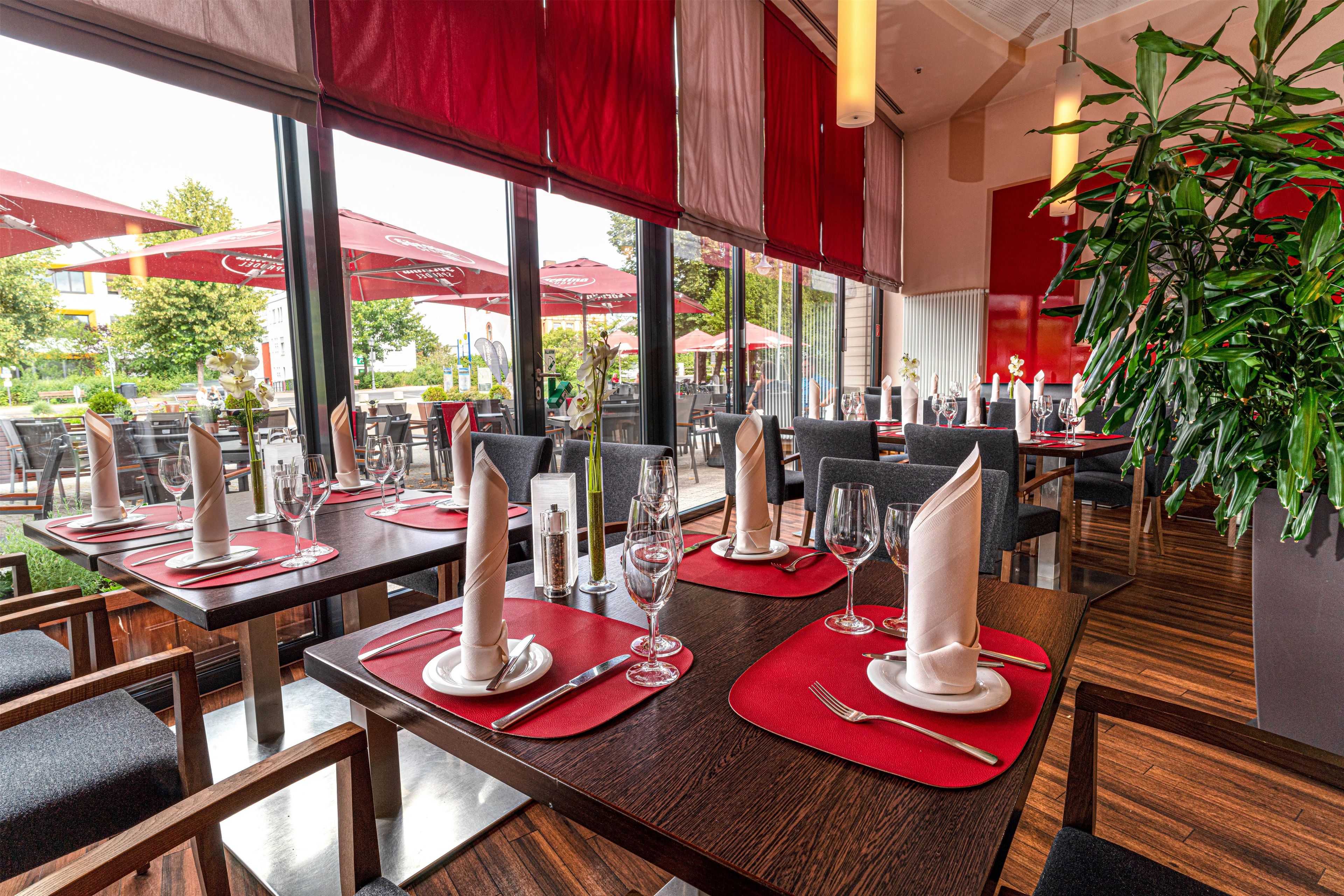 Un ristorante con tavoli apparecchiati, ampie finestre e piante da interno.