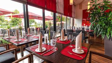 Un ristorante con tavoli apparecchiati, ampie finestre e piante da interno.