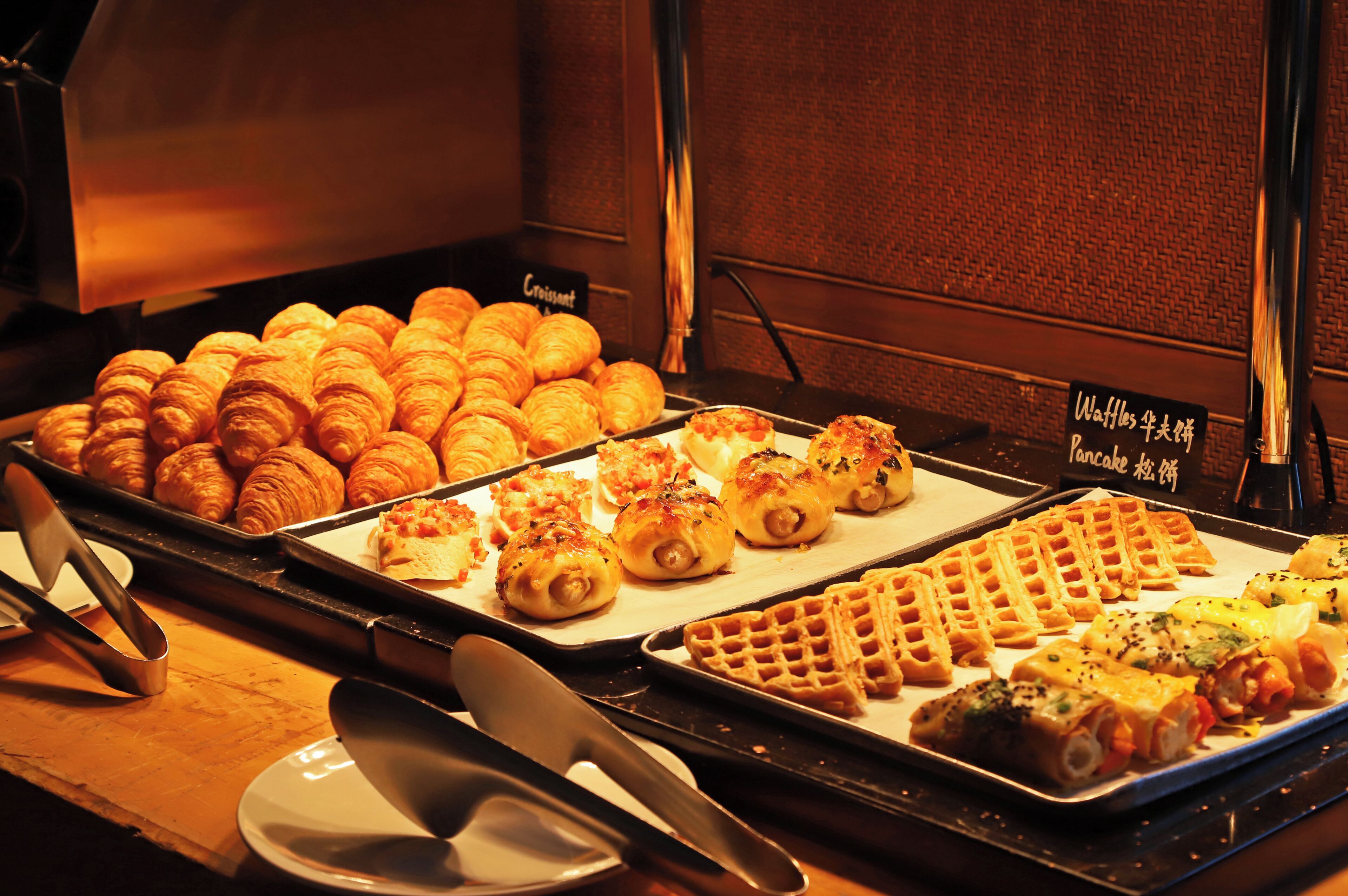 A buffet with croissants, pastries, and waffles.