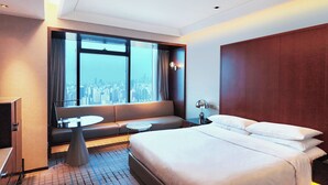 A hotel room with a large bed, a sofa, a small round table, and a view of a cityscape through a large window. - Renaissance Shanghai Zhongshan Park Skyline Hotel (Shanghai)