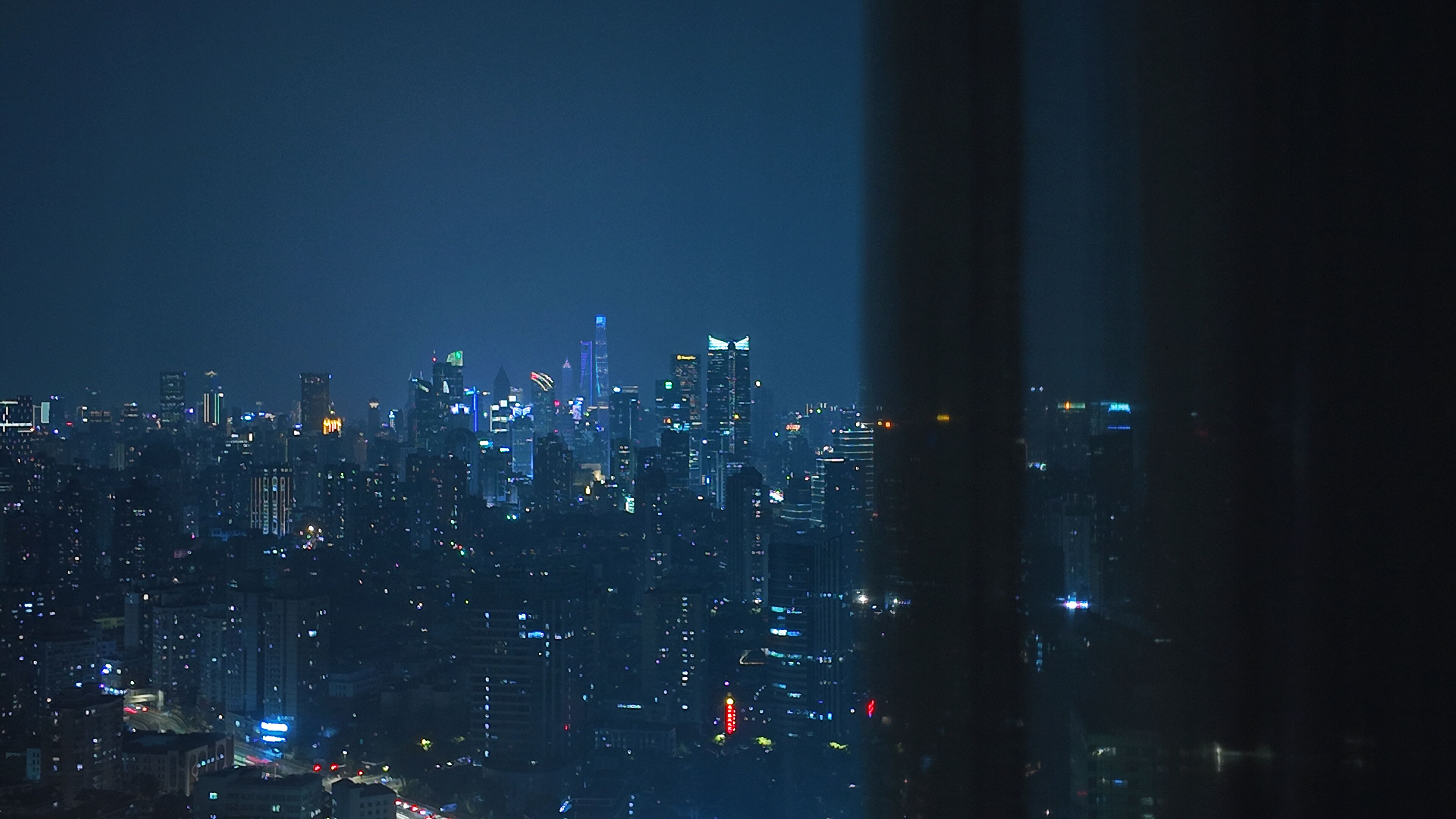 Un paisaje urbano nocturno con edificios iluminados y una vista a través de una ventana.