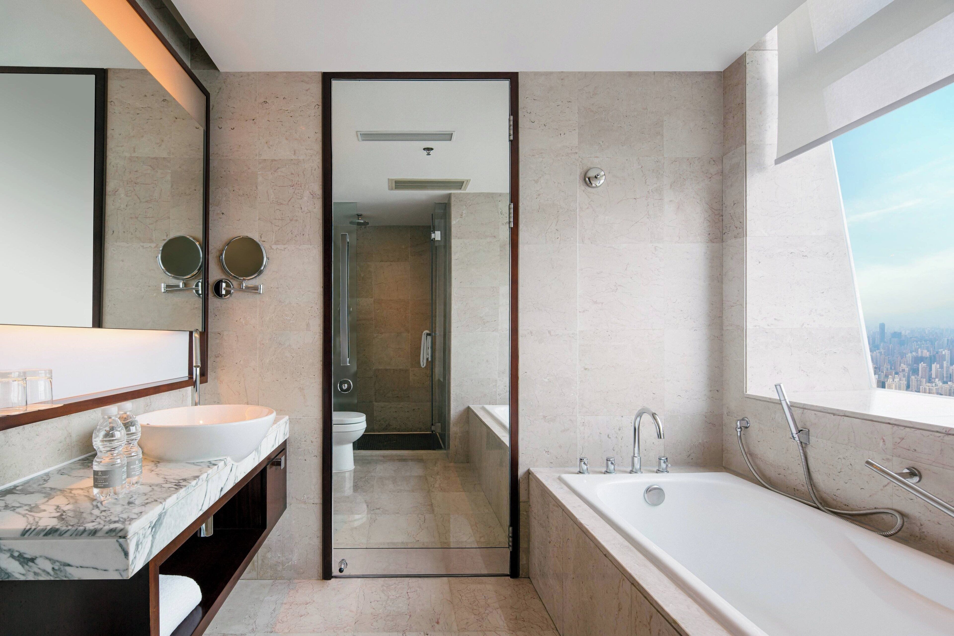 A modern bathroom with a large mirror, two round mirrors, a white sink, a bathtub, and a shower.