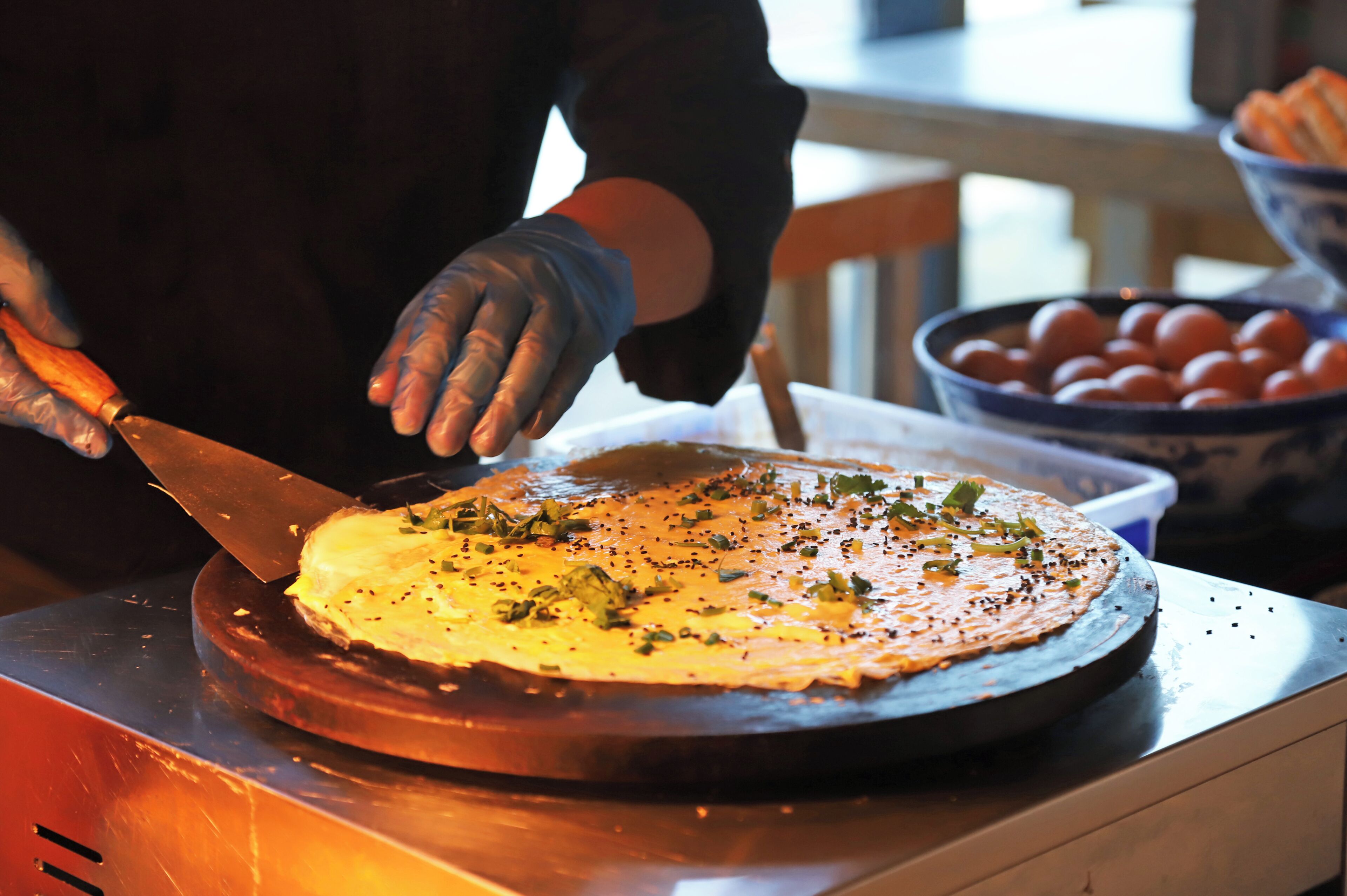 A person slicing a dish on a rotating platform, with a bowl of tomatoes in the background.