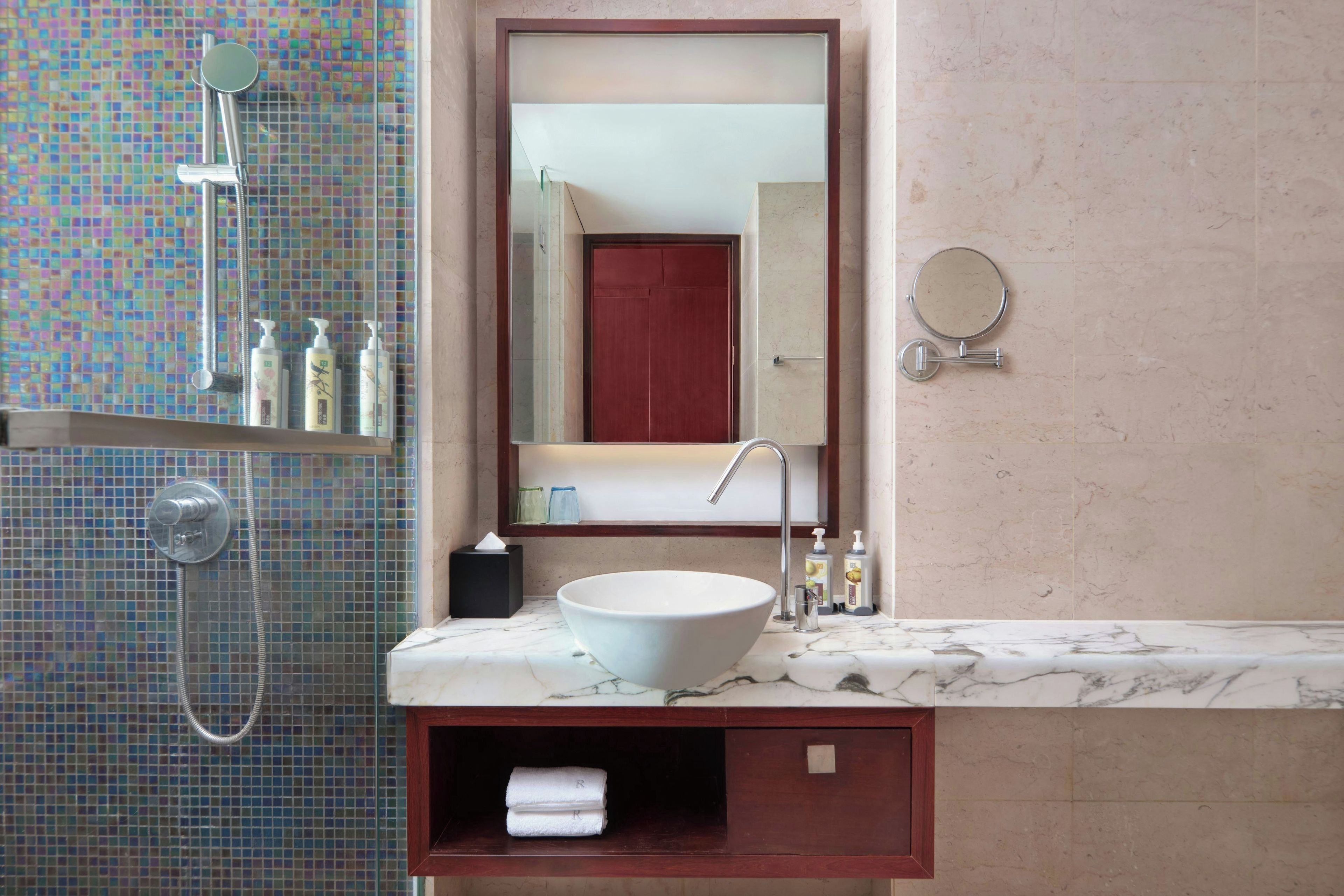 Un baño con lavamanos blanco, un espejo, un cabezal de ducha de mano y pared revestida de azulejos.