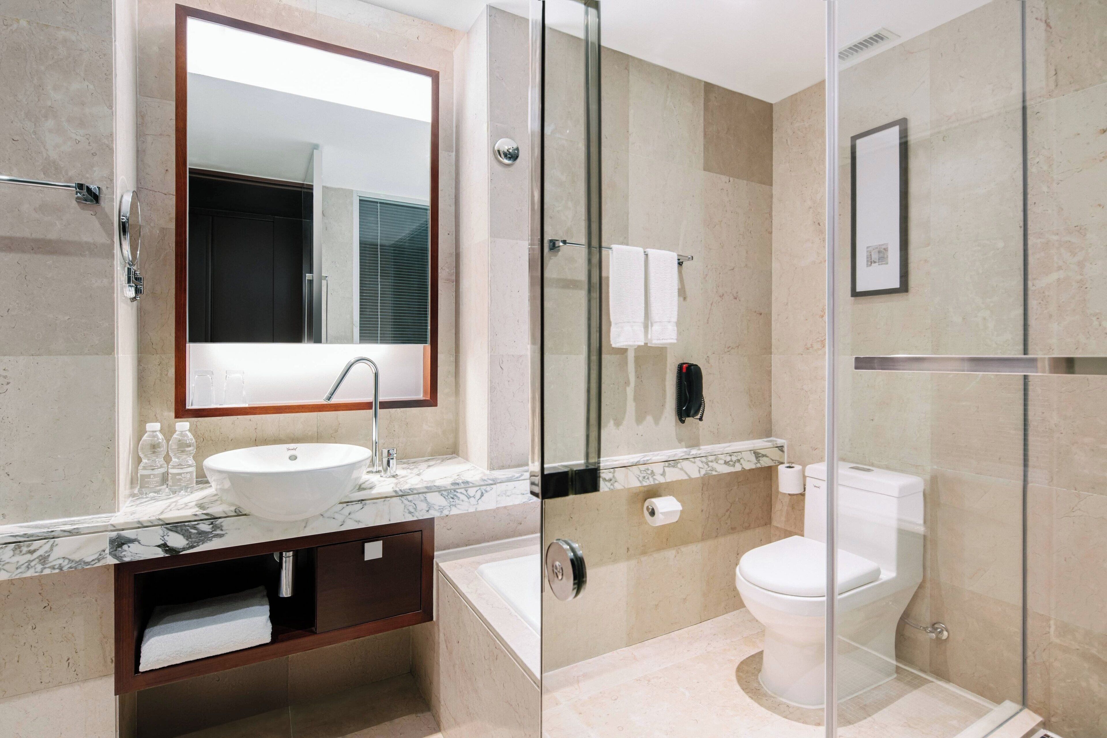A modern bathroom with a glass-enclosed shower, a sink with a marble countertop, and a toilet.