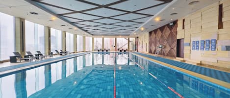 Une piscine intérieure à l’eau claire, avec un plafond laissant entrer la lumière du soleil et des chaises longues disposées le long des bords.