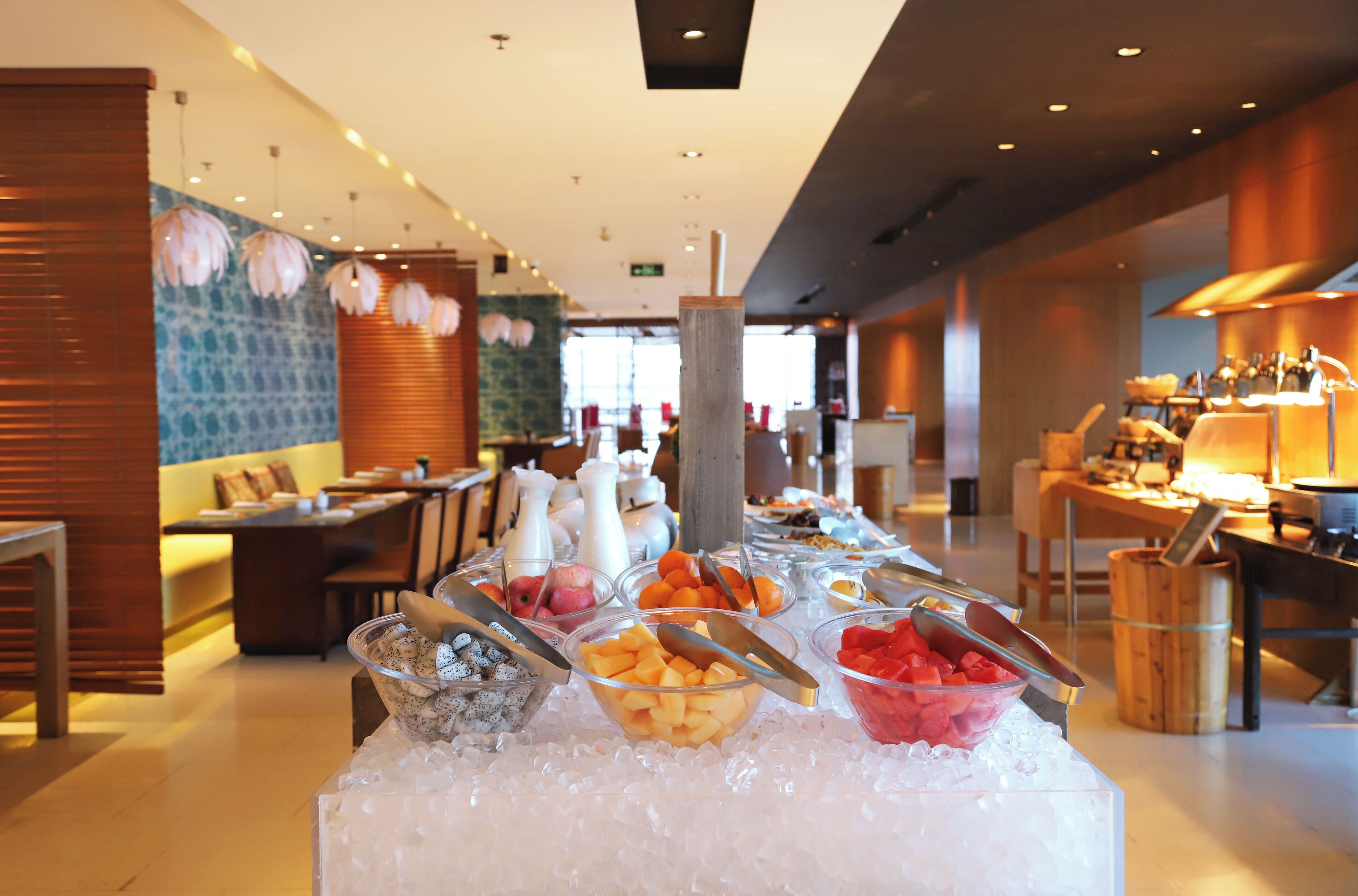 A buffet with various fruits and beverages on ice, a wooden bar area, and a seating area with tables and chairs.