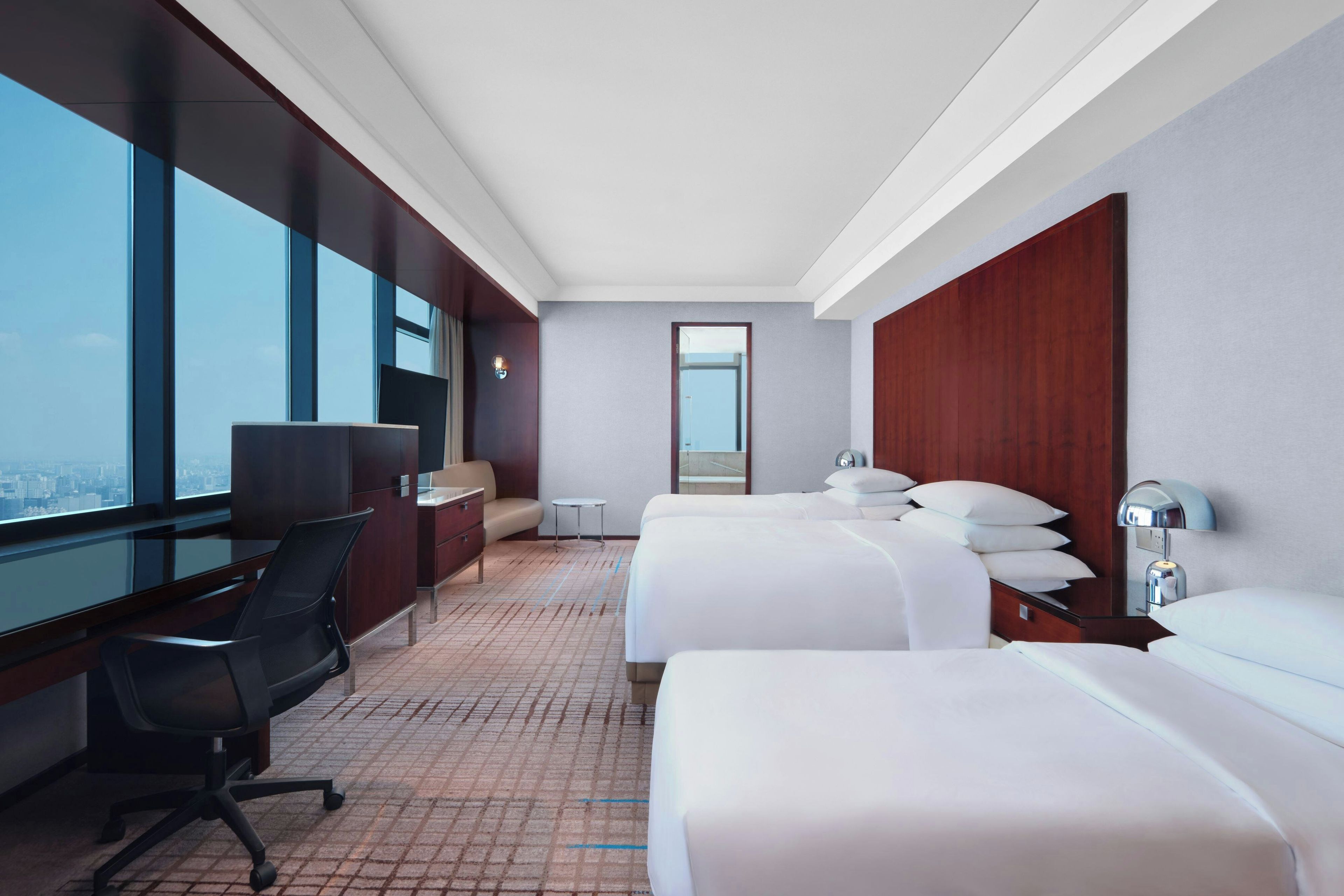 Een hotelkamer met een groot raam, een bureau, twee bedden en een klein tafeltje.