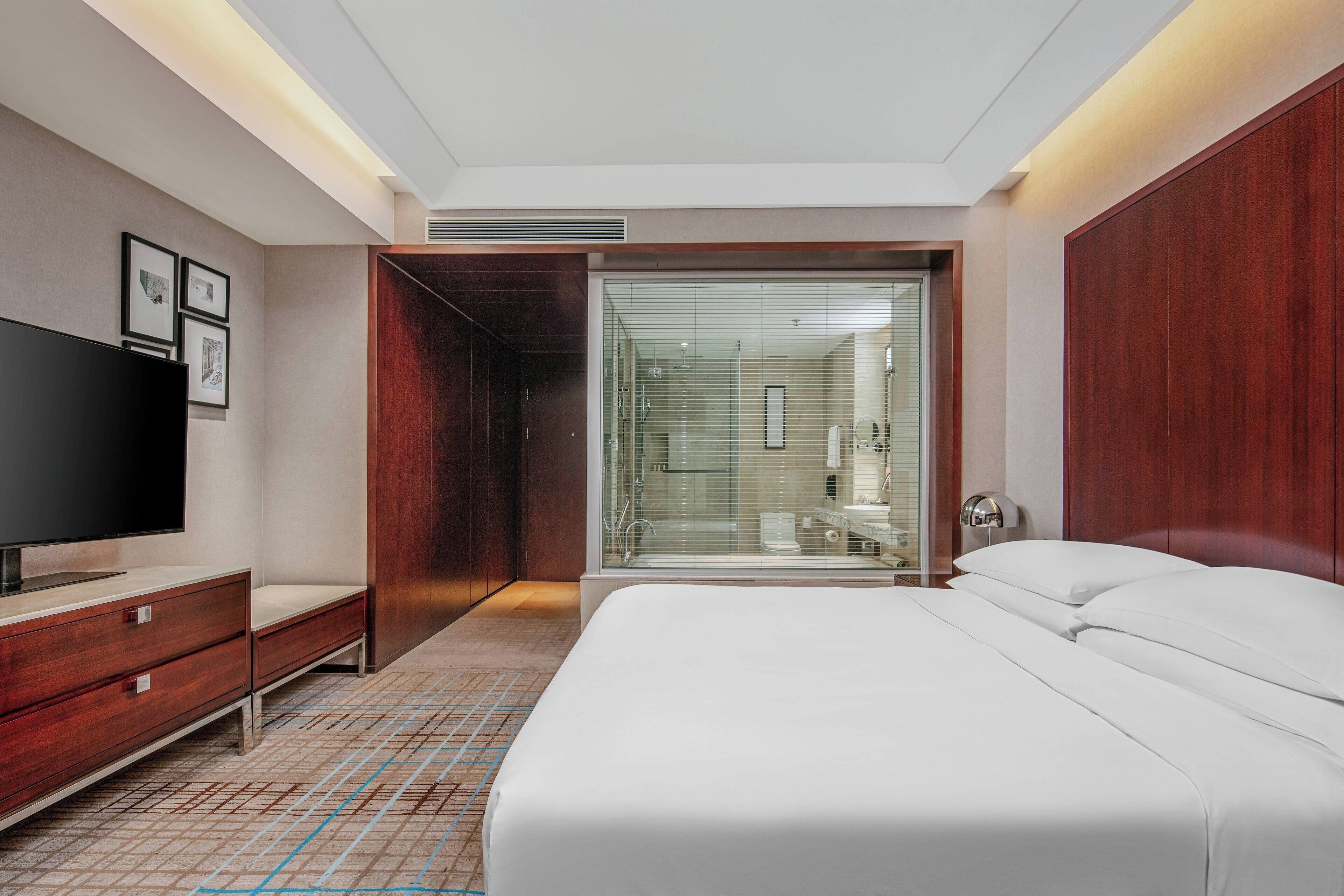 Una habitación de hotel moderna con una cama grande, televisión, armario y zona de ducha con mampara de vidrio.