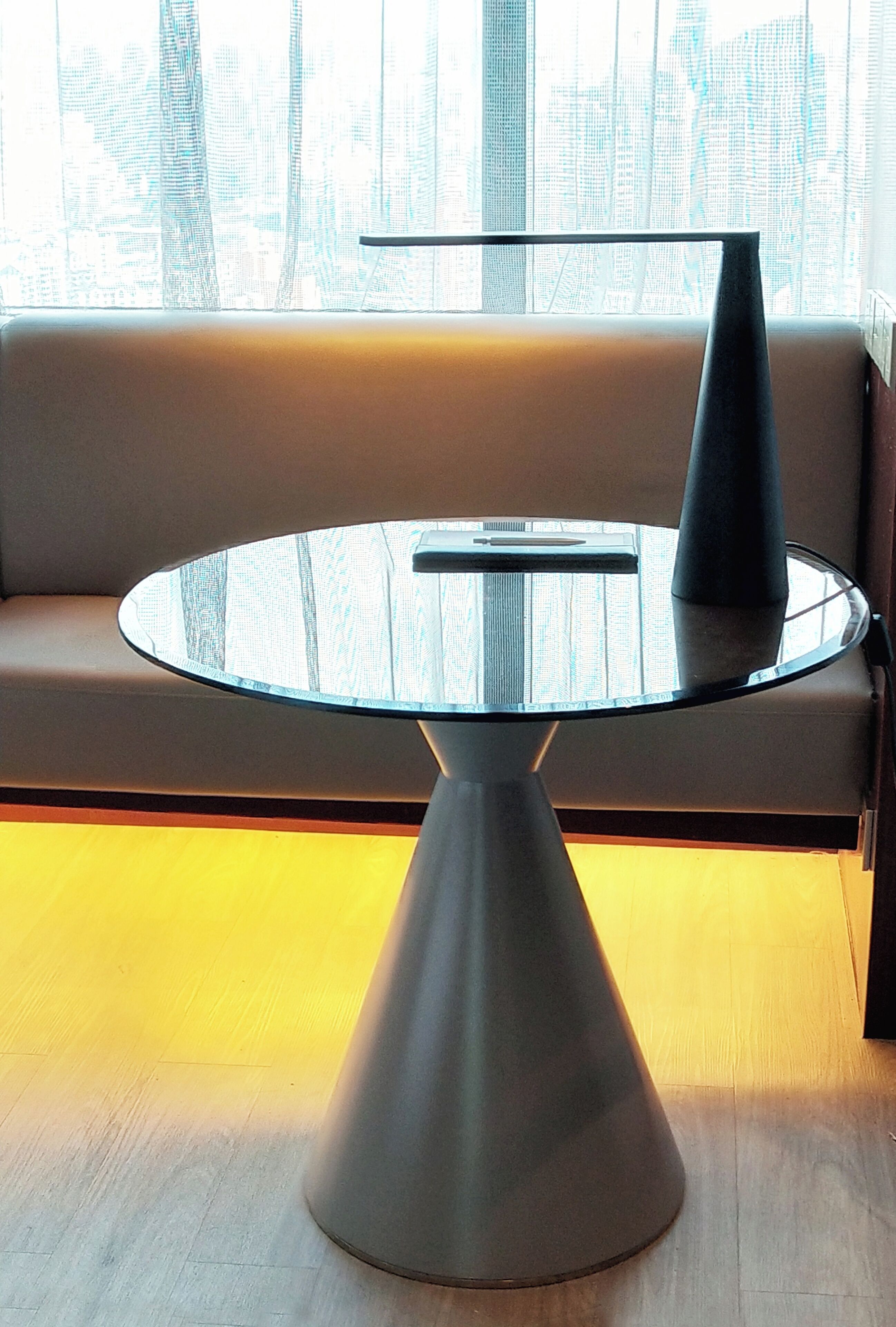 A round glass table with a metal base, positioned in front of a sofa with a city view through the window.