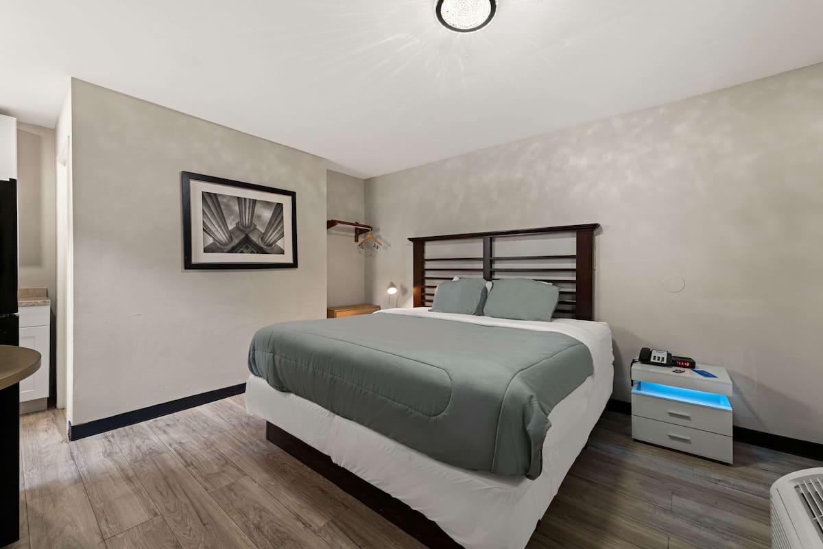 Un dormitorio con cama, mesita de noche, lámpara y un cuadro en la pared.
