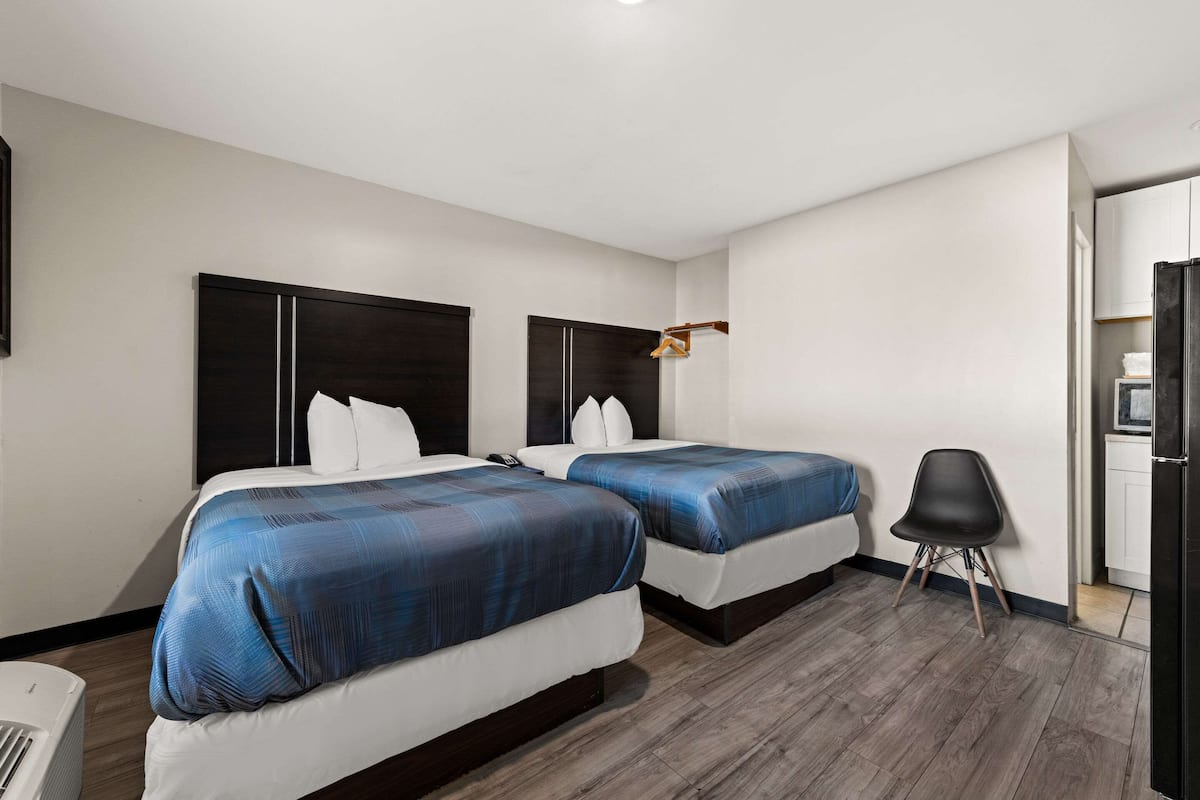 Habitación de hotel con dos camas, una silla, un escritorio y un armario.