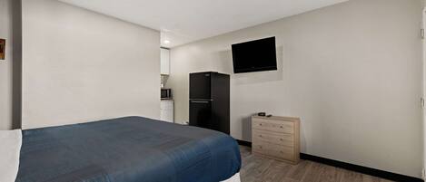 Ein Schlafzimmer mit einem Bett, einer Kommode, einem an der Wand befestigten Fernseher und einem Kühlschrank im Hintergrund.