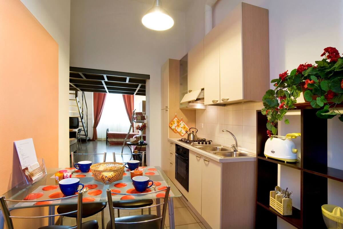 A compact kitchen with a dining area, featuring a table with chairs, a sink, and a toaster.