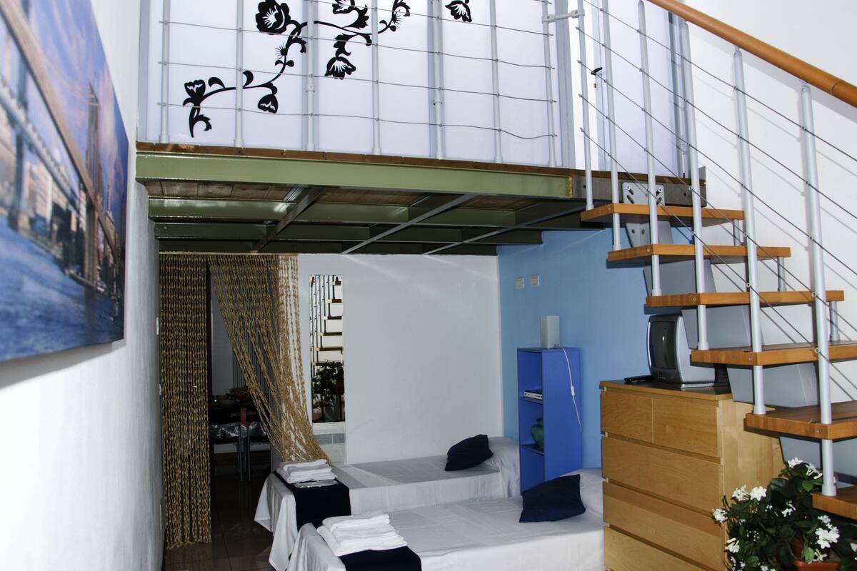 A room with a bed, a desk, a blue cabinet, and a staircase.