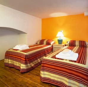 A hotel room with two beds, each with striped bedding, a nightstand with a lamp, and a wooden floor.