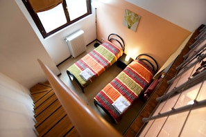 A dormitory room with two single beds, a radiator, a window, and a staircase.