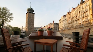 A terrace with wooden furniture and potted plants, overlooking a historic cityscape with a prominent tower and ornate buildings. - Boat Hotel Matylda (Prague)
