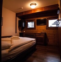 Quarto compacto com uma cama, uma escrivaninha pequena e uma televisão na parede.
