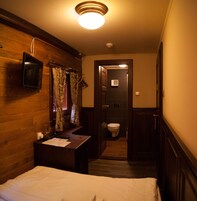 Hotellihuone, jossa on sänky, peilillä varustettu työpöytä, seinälle asennettu televisio ja ovi, joka johtaa kylpyhuoneeseen.