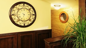 A wall clock with Roman numerals and a decorative frame, a wooden panel wall, a round mirror, and a potted plant. - Boat Hotel Matylda (Prague)