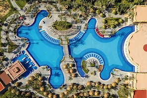Vista aérea de un complejo turístico con una gran piscina, palmeras y tumbonas.