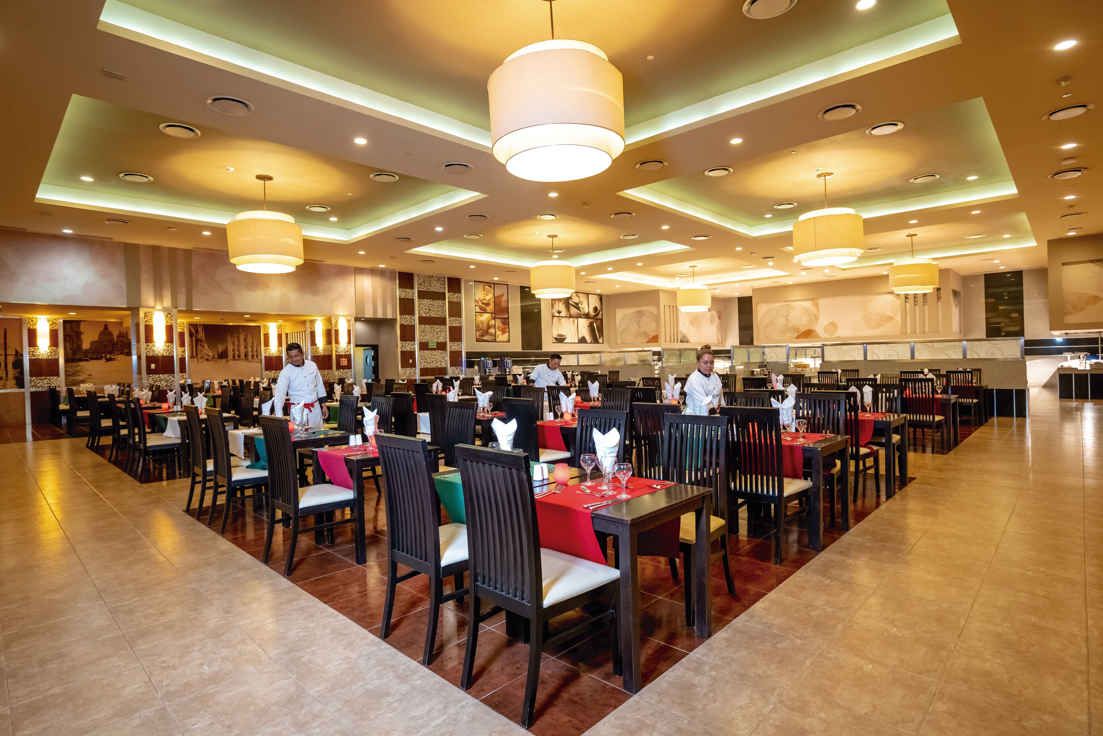 A spacious restaurant with multiple dining areas, each with tables and chairs, and a modern ceiling design with recessed lighting.
