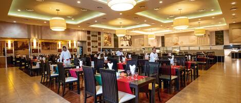 A spacious restaurant with multiple dining areas, each with tables and chairs, and a modern ceiling design with recessed lighting.