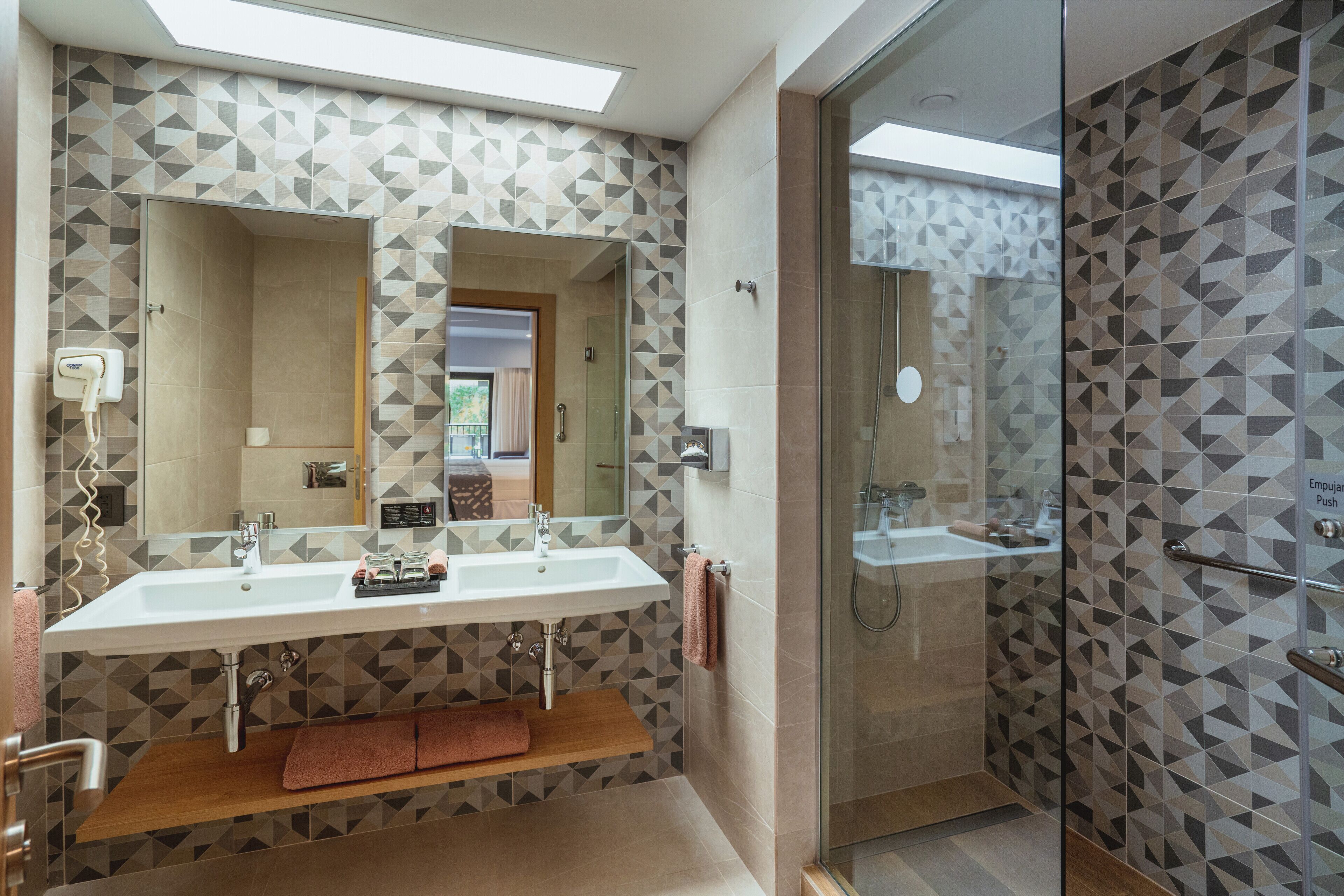 A modern bathroom with two sinks, a glass shower enclosure, and geometric patterned tiles.