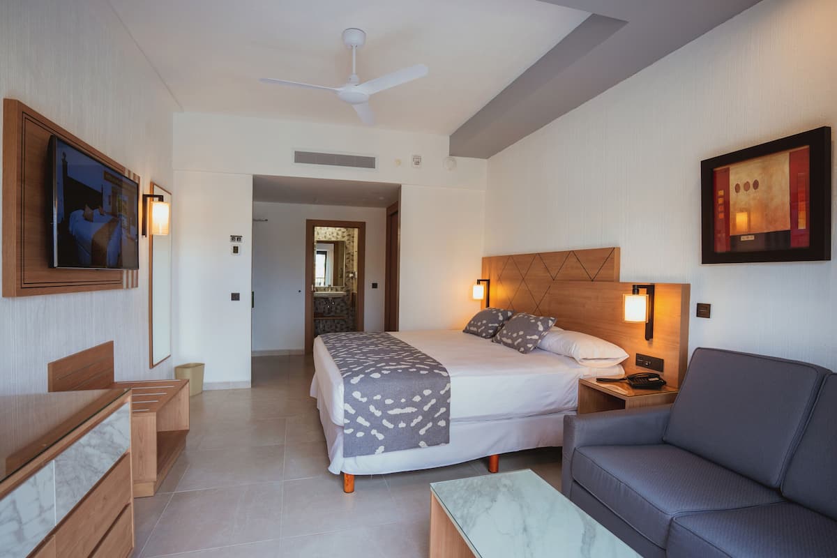 A hotel room with a bed, bedside table, lamp, and a sofa.
