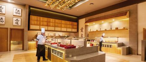 A modern restaurant interior with a central counter, wooden paneling, and a ceiling with floral decorations.