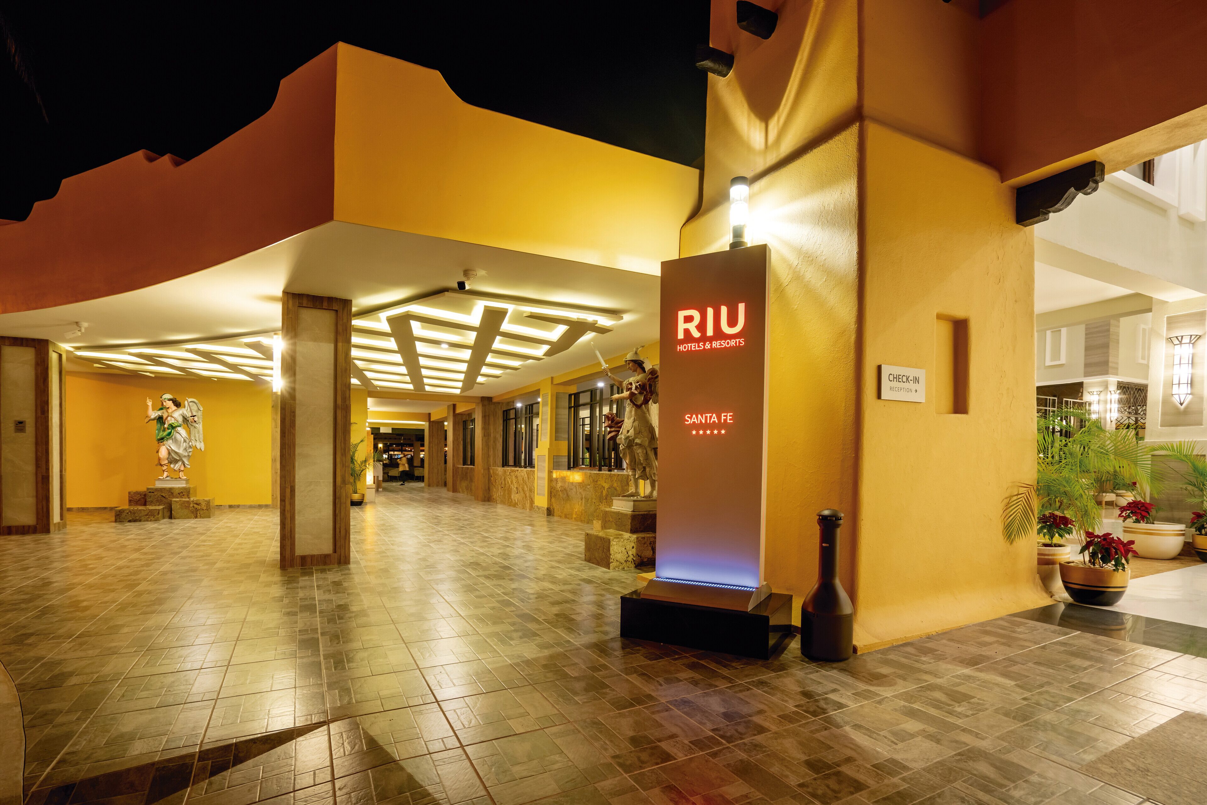 A hotel entrance with a check-in sign, a statue, and a tiled floor.