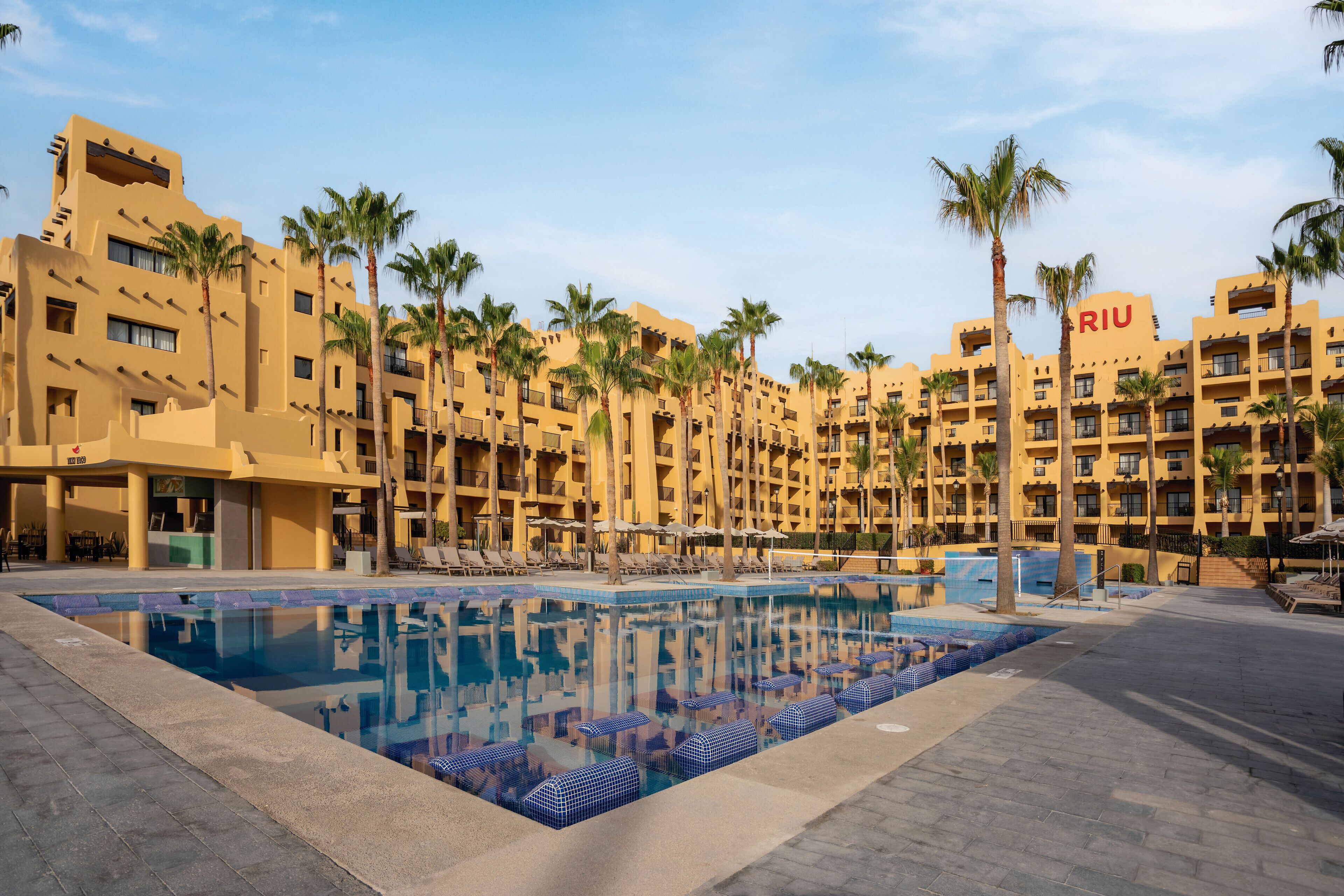 A hotel with a swimming pool surrounded by palm trees and sun loungers.