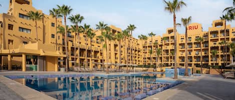 A hotel with a swimming pool surrounded by palm trees and sun loungers.