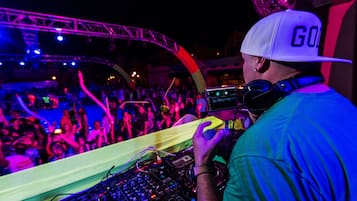 Un DJ actuando en un evento concurrido, con un escenario visible y público.