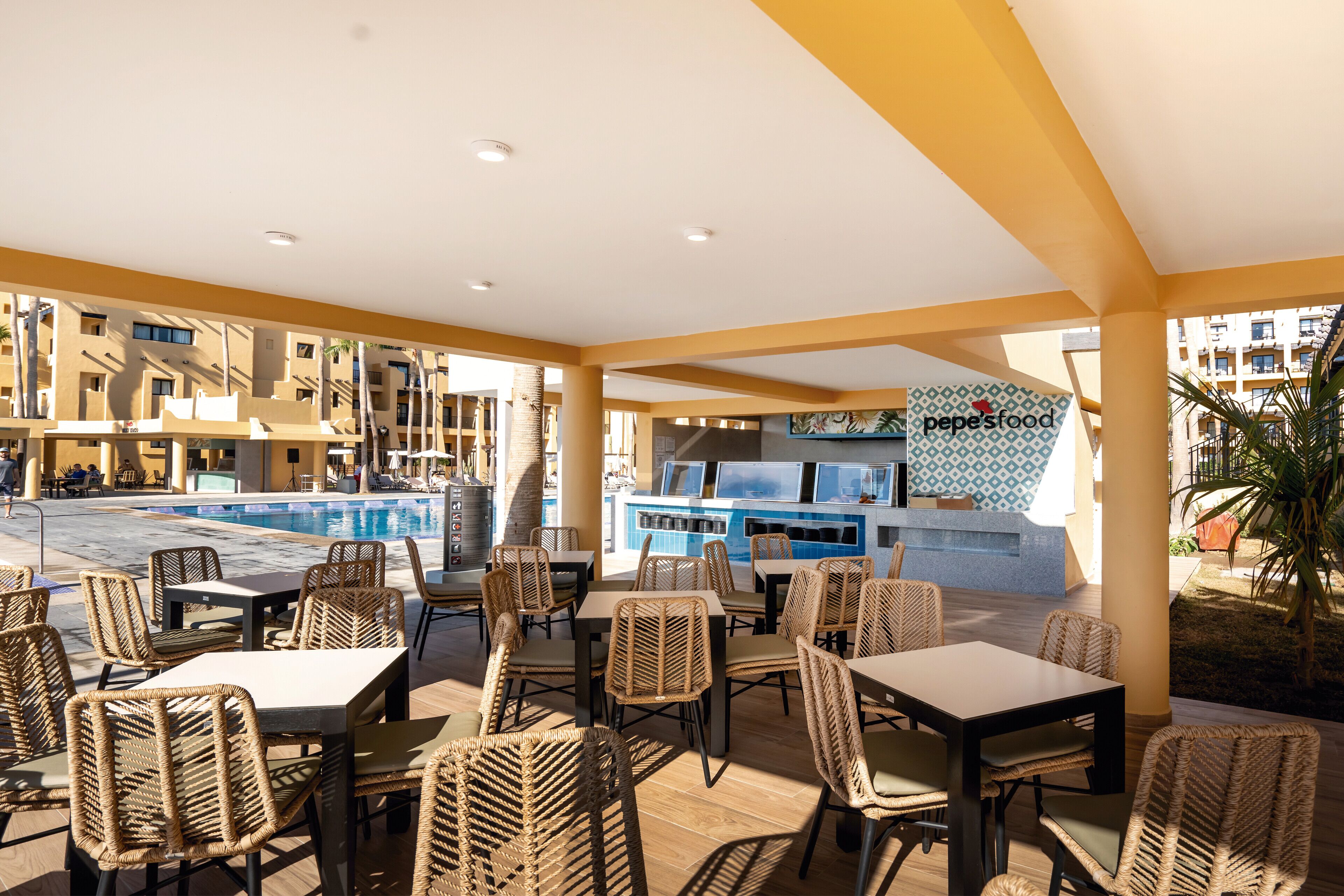 An outdoor dining area with wicker chairs and tables, a pool, and a food counter.