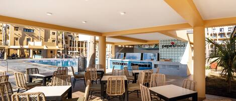 An outdoor dining area with wicker chairs and tables, a pool, and a food counter.
