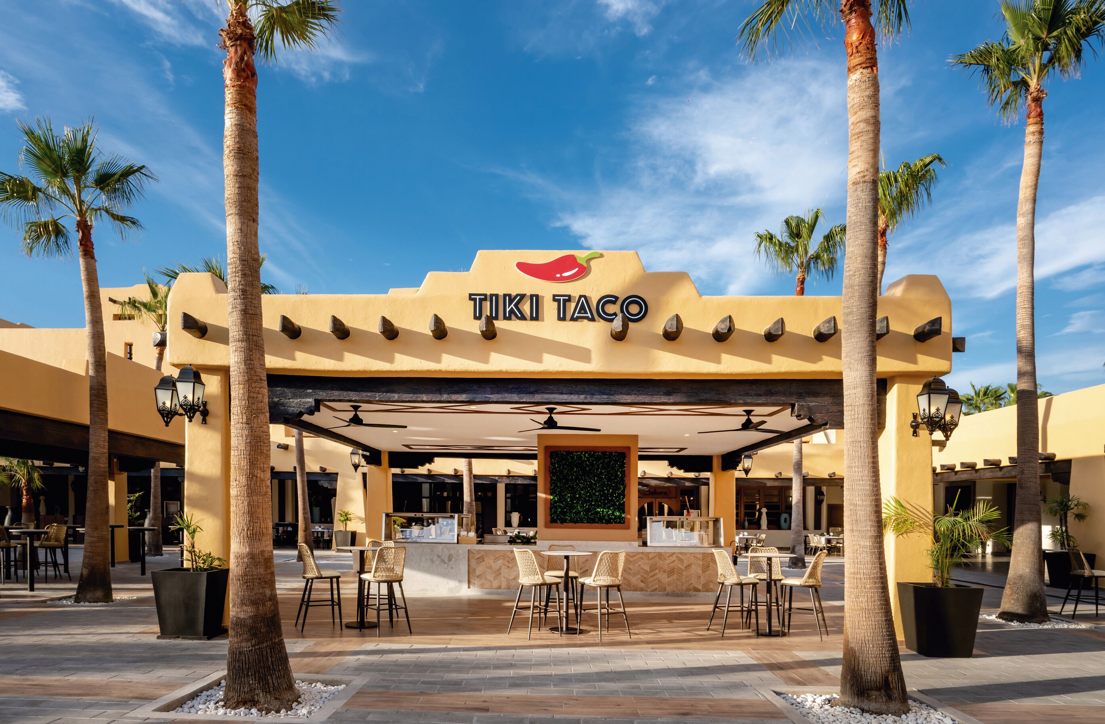 Ein TIKI TACO Restaurant mit Außenbereich, Palmen und blauem Himmel.