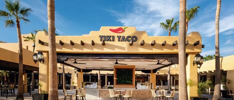 Ein TIKI TACO Restaurant mit Außenbereich, Palmen und blauem Himmel.