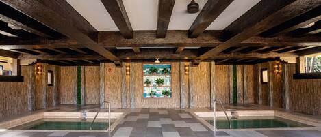A large indoor swimming pool with a checkered floor, wooden beams on the ceiling, and a decorative wall with plants.