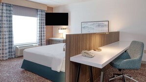 Une chambre d’hôtel comprenant un lit, un bureau avec un téléphone, une chaise, un téléviseur et un tableau encadré au mur.