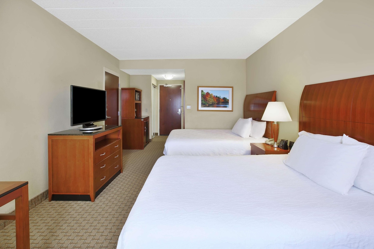 A hotel room with two beds, a TV, a desk, and a lamp.