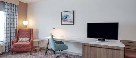 A hotel room with a desk, a television, a chair, and a lamp.
