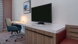 Une chambre d’hôtel équipée d’un bureau, d’une chaise, d’un téléviseur à écran plat, d’une lampe et d’un tableau au mur.